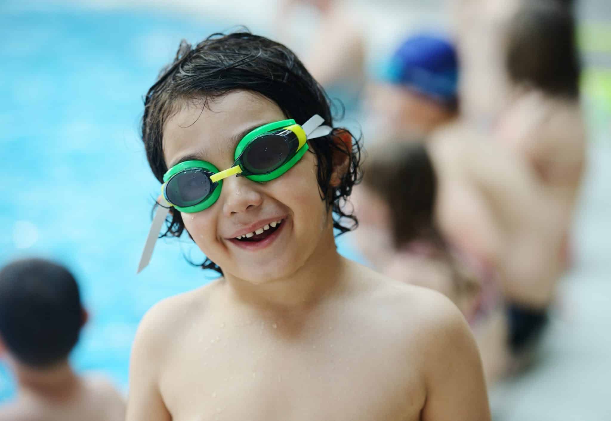 Child in swimming pool wearing green goggles enjoying a fun pool day.