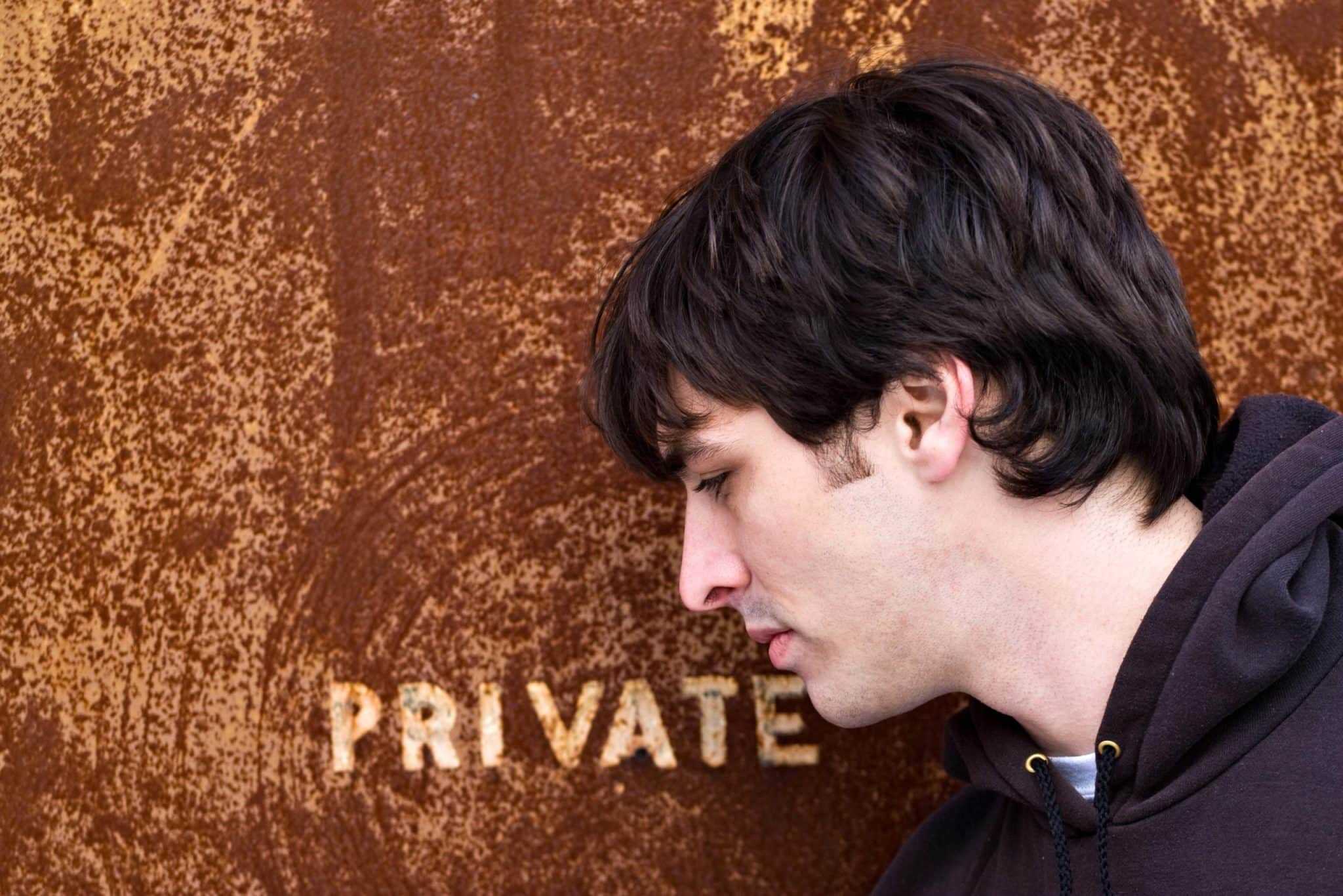 Teenager with head bowed near rusted "PRIVATE" sign, representing privacy concerns.
