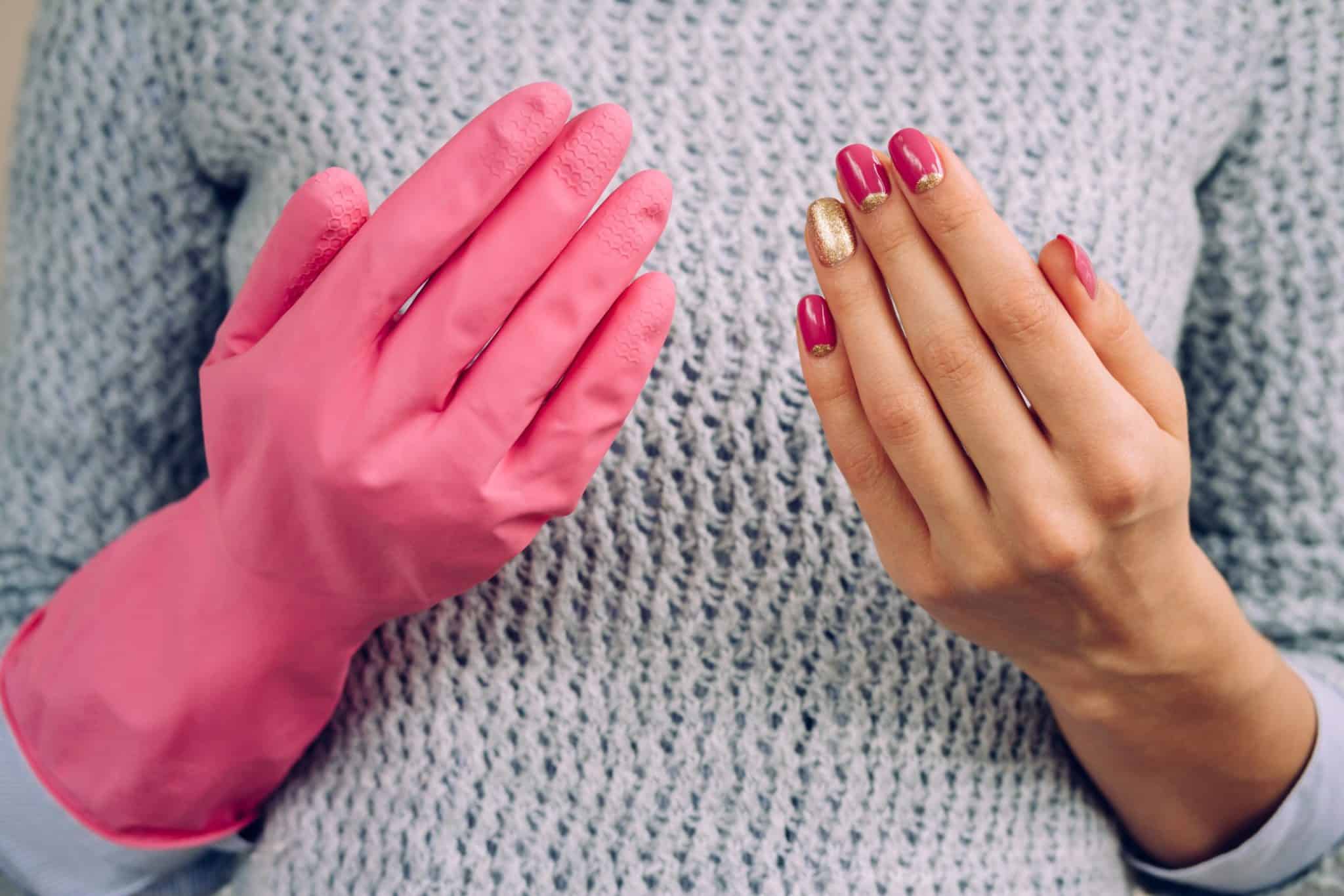 Bright pink cleaning glove on hand, woman showing off her manicured nails, close-up of hands and sweater.